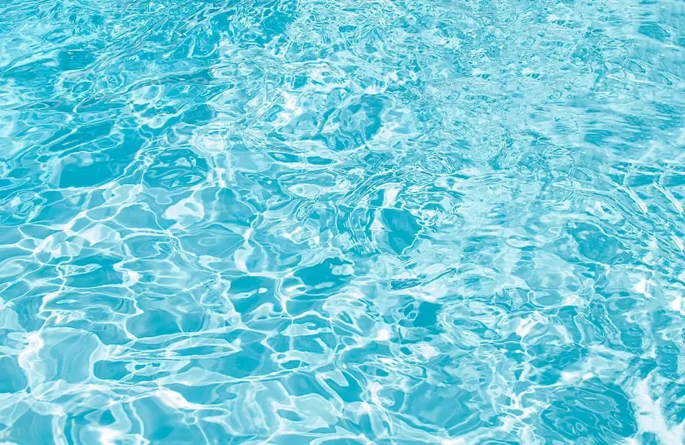 Gros plan sur la surface ondulée de l'eau d'une piscine, reflets et nuances de bleu turquoise