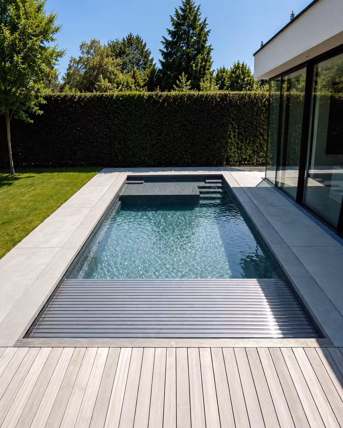 Piscine coque rectangulaire avec volet roulant immergé en cours de fermeture, deck bois et terrasse pierre