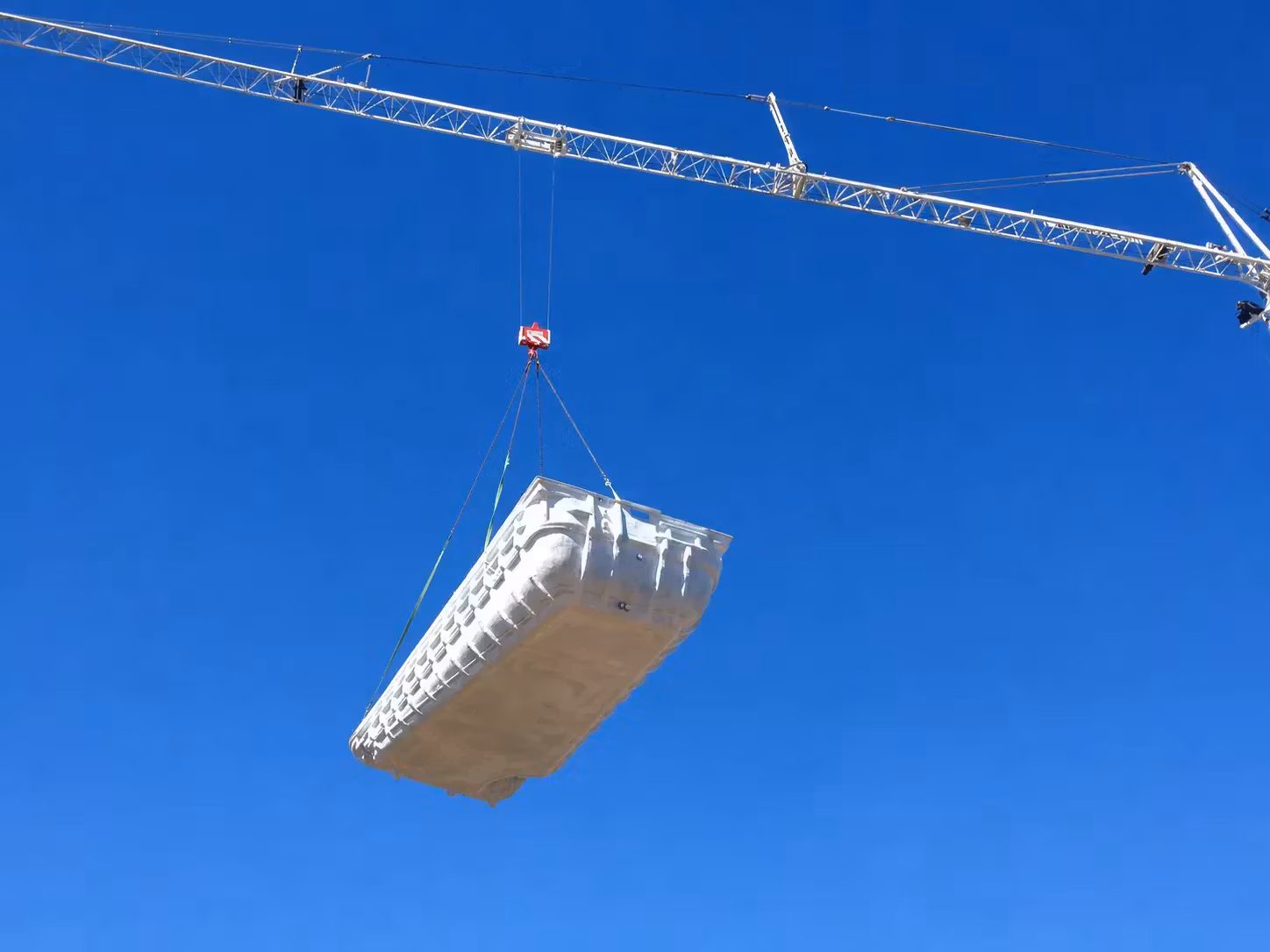 Coque polyester de piscine suspendue à une grue lors d'une livraison à Marseille, ciel bleu dégagé