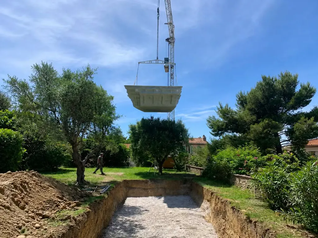 Coque polyester déposée par grue dans un terrain creusé, jardin planté d'oliviers