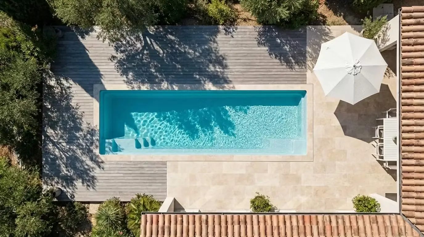 Vue aérienne d'un couloir de nage intégré à une terrasse en pierre claire avec deck en bois et parasol