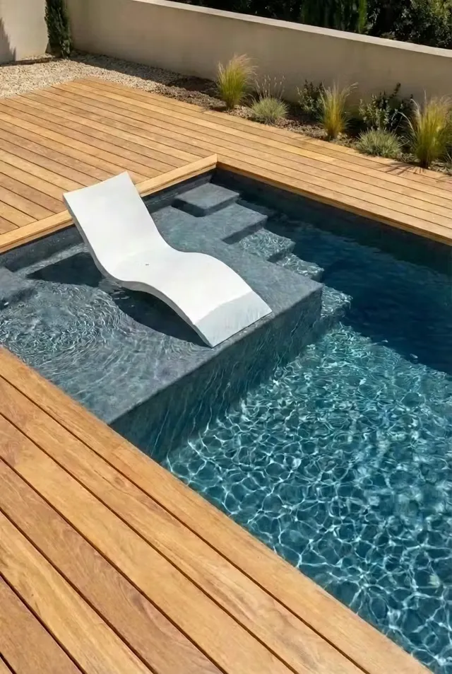 Bain de soleil immergé sur la plage d'une piscine coque revêtement gris, deck bois clair en bordure
