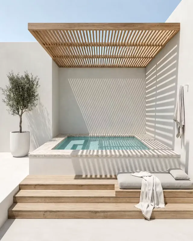 Mini-piscine surélevée bordée de pierre claire, olivier en pot et pergola bois projetant des ombres rythmées