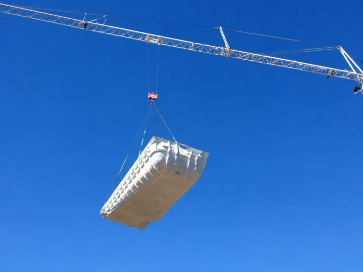 Coque polyester de piscine suspendue à une grue lors d'une livraison à Marseille, ciel bleu dégagé